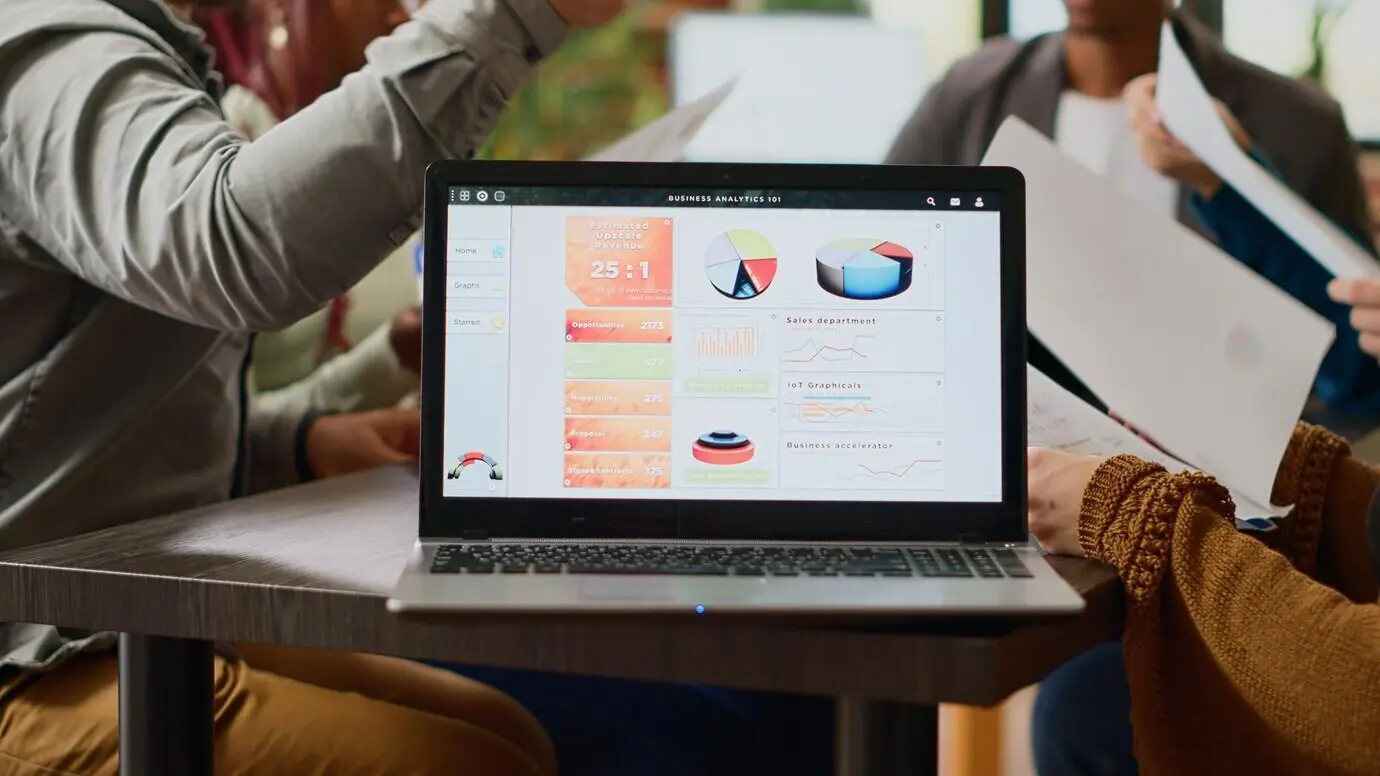 Многонациональная группа коллег анализирует в программном обеспечении на ноутбуке бизнес-диаграммы и данные инфографики. Люди выполняют командную работу по созданию бумажных обзоров и профессионального отчёта. Крупный план.